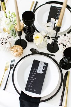 the table is set with black and white plates, silverware, and gold place settings