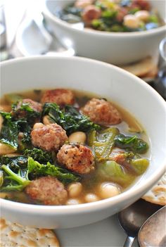 two bowls of soup with meatballs, spinach and crackers on the side