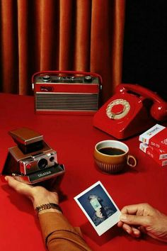 a person holding an old fashioned camera next to a red table with other items on it