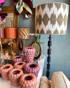 a table topped with lots of different colored vases next to a lamp and mirror