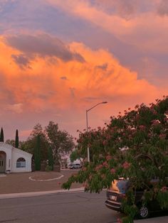 the sky is pink and orange as the sun sets over a small white building with trees in front of it