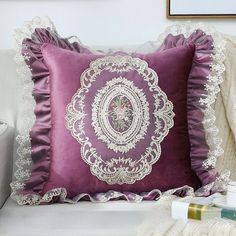 a purple pillow on a white couch with lace trim around the edges and an embroidered design