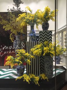 yellow flowers are in vases on display at a store window with other items behind them