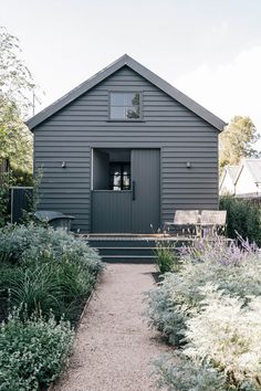 a small gray house sitting next to a lush green field