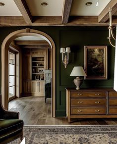 a living room with green walls and wooden furniture in the center, along with an arched doorway leading to another room