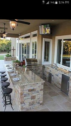 an outdoor kitchen with bar stools and several lights on the outside wall next to it