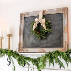 a chalkboard with a wreath hanging on it's mantle next to two candles