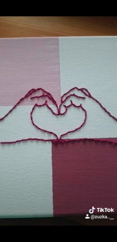 two hands making a heart with yarn on a piece of fabric that is pink and white