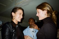 two women standing next to each other and one holding a wine glass in her hand