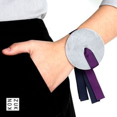 a woman's hand wearing a purple and black tie around her wrist with a silver disc on it