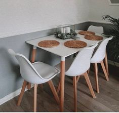 a dining table with four chairs and place mats on the top, next to a potted plant