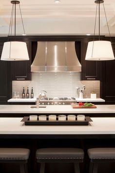 a large kitchen with black cabinets and white counter tops, two pendant lights hanging over the island