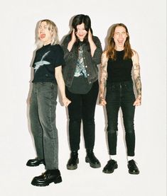 three women standing next to each other in front of a white wall with tattoos on their arms