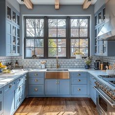 a kitchen with blue cabinets and wood flooring is pictured in this image, there are windows that look out onto the street