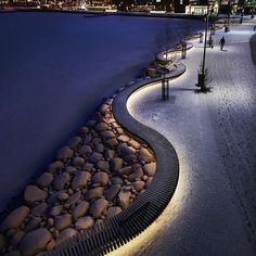 a snowy landscape with rocks and lights in the foreground, along side a body of water at night