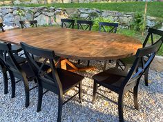 a large wooden table surrounded by black chairs and graveled area with stone wall in the background