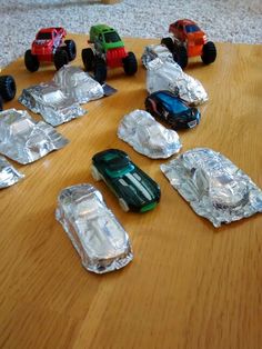 toy cars are sitting on aluminum foil wrapped in plastic wrappers and placed on a wooden table