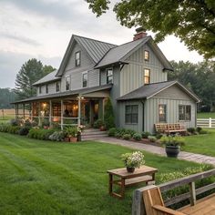 a large gray house sitting in the middle of a lush green field next to a wooden bench