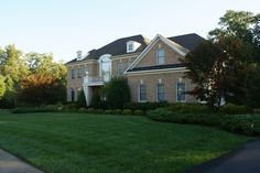 a large brick house sitting in the middle of a lush green field with lots of trees