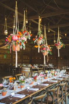 the tables are set up for an event with hanging vases and flower centerpieces