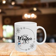 a white coffee mug with the words hello winter on it sitting on a wooden table