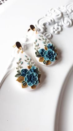 two white and blue flowers are hanging from the side of a cake plate on a table