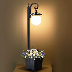 a lamp that is on top of a table with flowers in the pot underneath it