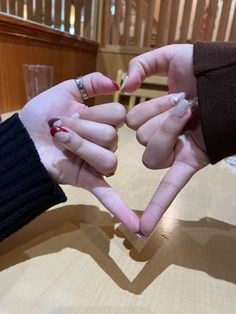 two people making a heart shape with their hands on top of each other at a table