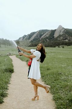 a woman in white shirt and shorts holding a water hose while standing on dirt path