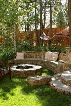 a stone fire pit in the middle of a grassy area with hammock hanging above it