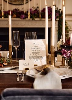 a place setting with candles and menus on the table in front of a fireplace