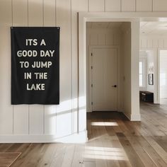 a black and white banner hanging on the wall in a room with wood flooring that says, it's a good day to jump in the lake