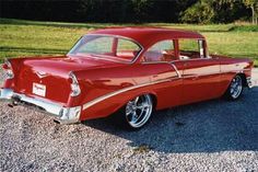 an old red car is parked on the gravel