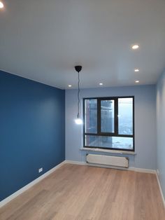 an empty room with blue walls and wooden floors, including a radiator in the corner