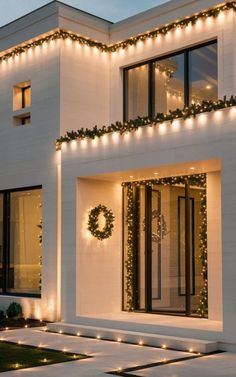 a white house with christmas lights on the front and side windows, decorated with wreaths