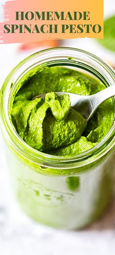 a jar filled with green pesto on top of a white table next to leaves