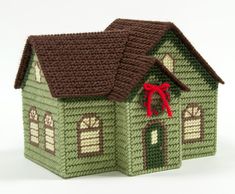 a knitted green house with a red bow on the roof and windows is shown