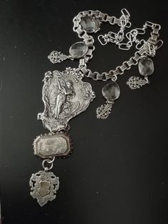 The central pendant in this assemblage is an art nouveau plaque in plated silver that most likely adorned the back of a mirror. It supports an antique Victorian aesthetic movement sterling brooch featuring a flying swallow. From the brooch is a hallmarked British sterling Victorian era watch fob with a gilded initialed cartouche. Accompanying pendants are rhodium plated bezel set free form faceted crystals and Victorian inspired filigree charms. All elements are attached to silver plated book chain and the necklace is finished with larger links and a hook so you can adjust the length. Victorian Silver Necklace With Antique Finish, Art Deco Silver Jewelry With Vintage Charm, Silver Art Deco Jewelry With Vintage Charm, Silver Medallion Art Deco Jewelry, Silver Art Deco Medallion Necklace, Elegant Silver Medallion Brooch, Victorian Silver Necklace For Collectible, Victorian Silver Necklace, Silver Art Nouveau Brooch