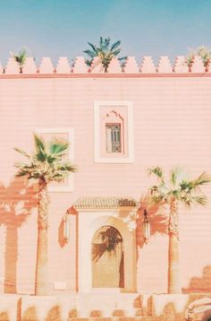 a pink building with palm trees in front of it and a car parked on the street