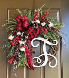 a wreath with the letter j on it and pine cones, berries, and evergreens