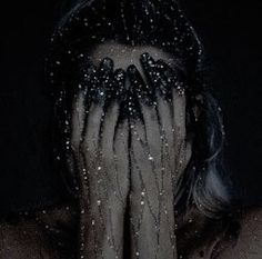 a woman with her hands on her face covered in beads and black nail polishes