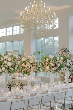 a room filled with lots of tables covered in white linens and tall centerpieces