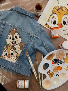 a denim jacket with chipmuns painted on it and paintbrushes next to it