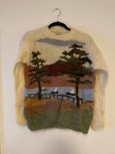 a sweater hanging on a white wall with trees and clouds painted on it's back