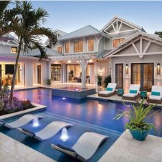 an outdoor swimming pool with lounge chairs and palm trees in front of the house at dusk