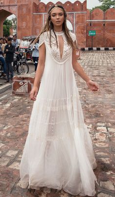 a woman in a long white dress standing on a brick walkway with people behind her