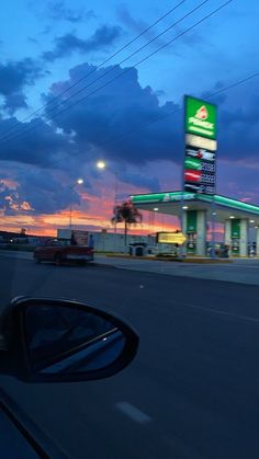 a gas station at dusk with cars passing by