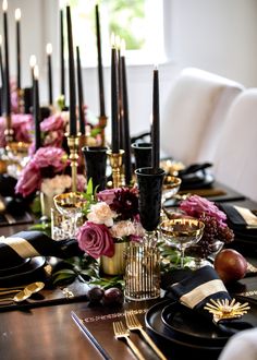 the table is set with black and gold place settings, flowers, candles, and fruit