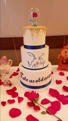 a three tiered cake sitting on top of a table covered in red rose petals