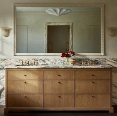 an image of a bathroom setting with marble counter tops and wooden cabinets in front of a large mirror